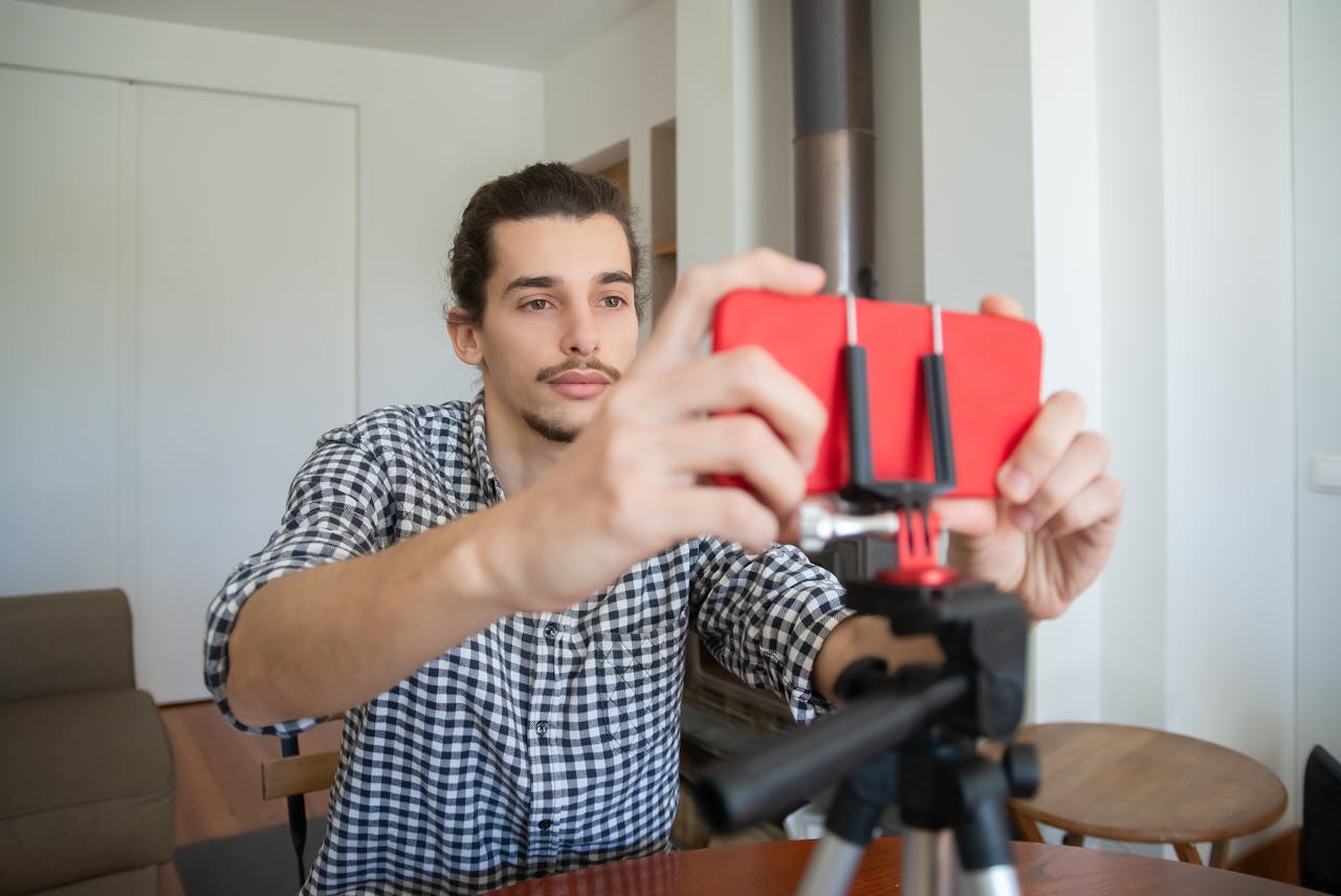 Confident young man adjusting smartphone on tripod for home vlogging setup.